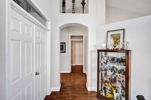 hall featuring arched walkways, dark wood-style flooring, and baseboards