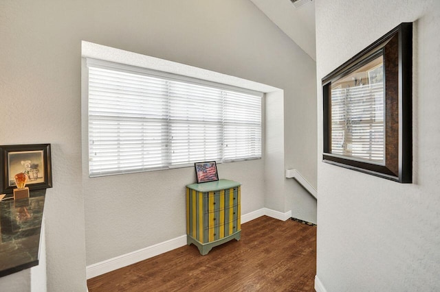 hallway featuring wood finished floors, healthy amount of natural light, vaulted ceiling, and baseboards