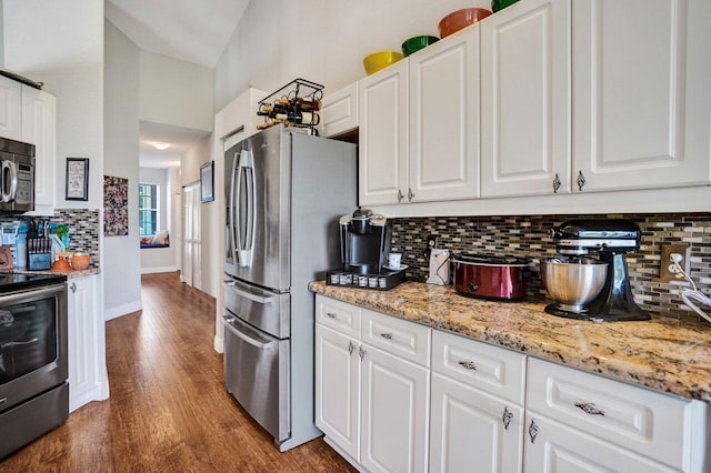 kitchen with appliances with stainless steel finishes, decorative backsplash, white cabinets, dark wood finished floors, and light stone counters