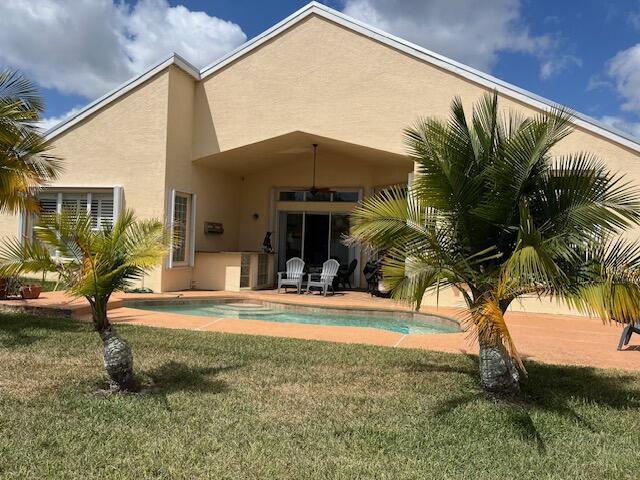 212 NW Pleasant Grove Way, Port Saint Lucie, FL 34986 - rear view of property featuring stucco siding, a yard, and an outdoor pool
