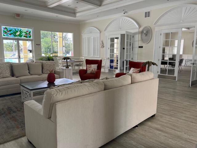 living area featuring visible vents, ornamental molding, wood finished floors, and coffered ceiling