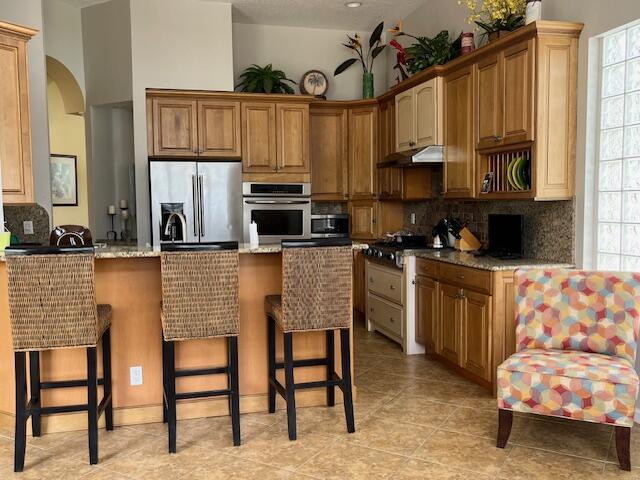kitchen with a peninsula, a kitchen breakfast bar, under cabinet range hood, appliances with stainless steel finishes, and backsplash