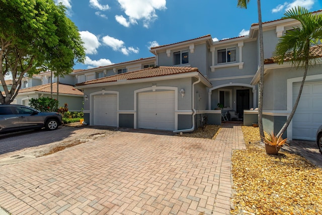 mediterranean / spanish house with a garage, decorative driveway, stucco siding, and a tile roof