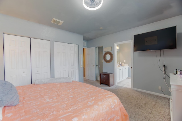 bedroom with visible vents, light colored carpet, baseboards, multiple closets, and ensuite bath