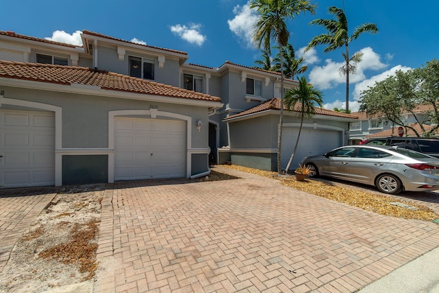 mediterranean / spanish home featuring a tiled roof, decorative driveway, a garage, and stucco siding
