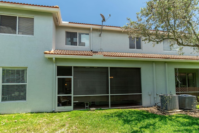 rear view of house with a lawn, central AC unit, a sunroom, and stucco siding
