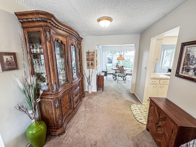 corridor featuring light colored carpet, a textured ceiling, and baseboards