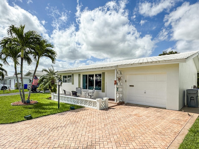 ranch-style home with a garage, a front lawn, covered porch, decorative driveway, and stucco siding