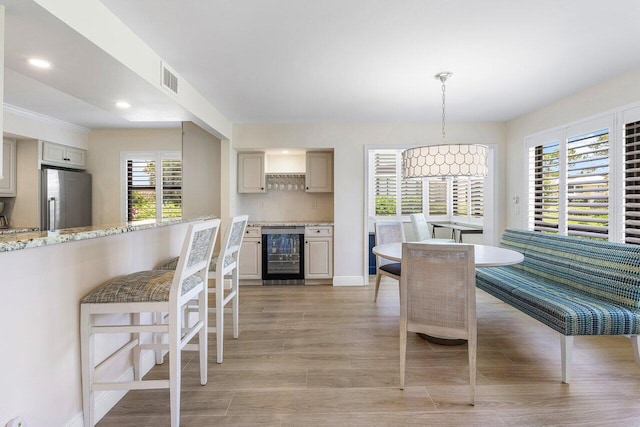 dining area featuring beverage cooler, visible vents, a wealth of natural light, and light wood-style flooring
