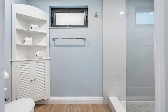 full bathroom with wood finished floors, toilet, and tiled shower