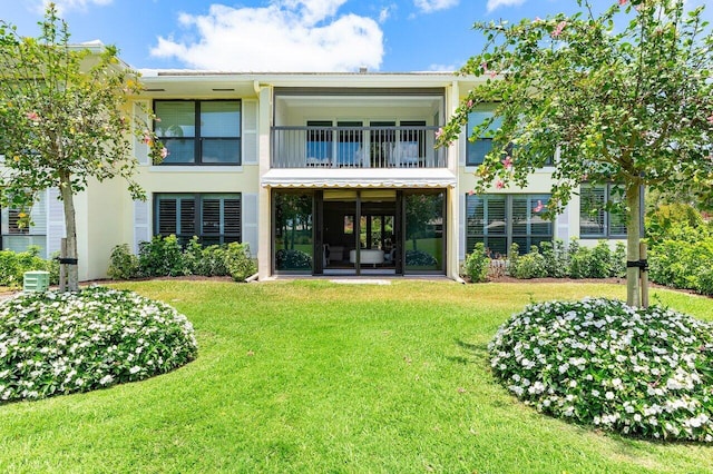 rear view of property with a lawn, stucco siding, and a balcony