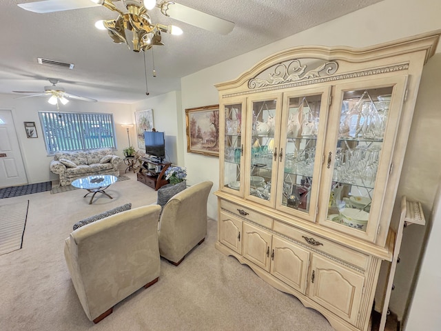 living room featuring light carpet, ceiling fan with notable chandelier, a textured ceiling, and visible vents