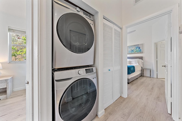washroom featuring baseboards, laundry area, light wood finished floors, and stacked washer / dryer