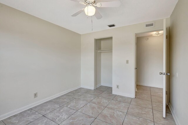 unfurnished bedroom with light tile patterned flooring, a closet, a ceiling fan, and baseboards