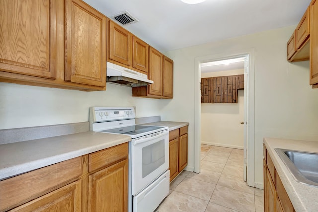 kitchen featuring electric stove, under cabinet range hood, light countertops, light tile patterned floors, and a sink