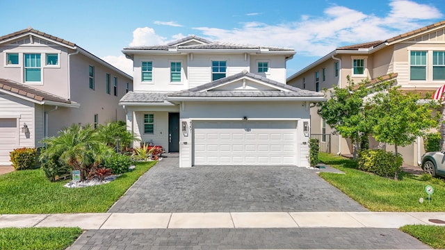traditional-style house with an attached garage, a front lawn, a tile roof, stucco siding, and decorative driveway