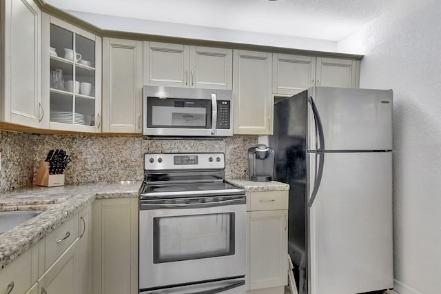 9214 Flynn Cir # 6, Boca Raton, FL 33496 - kitchen featuring light stone countertops, appliances with stainless steel finishes, decorative backsplash, and glass insert cabinets