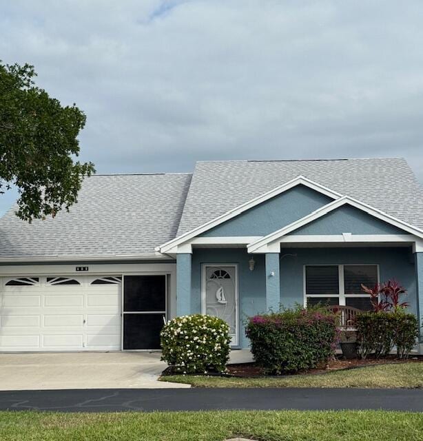 view of front facade featuring roof with shingles, covered porch, an attached garage, and driveway