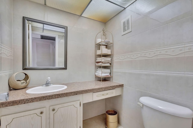half bath featuring tile walls, vanity, toilet, and visible vents