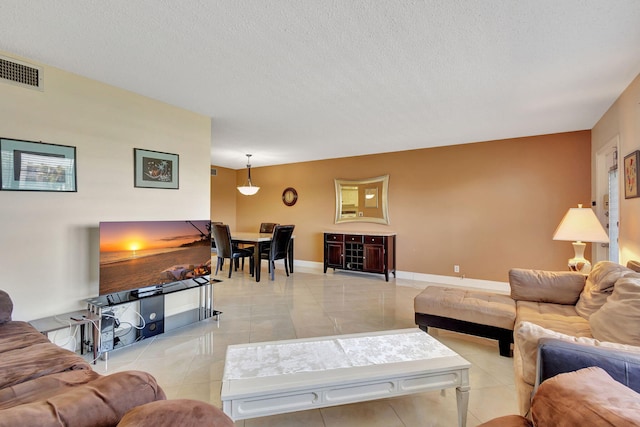 living room featuring baseboards, light tile patterned flooring, a textured ceiling, and visible vents