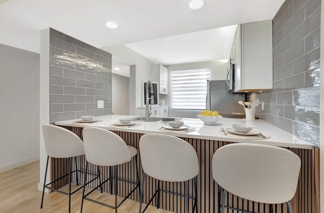6049 Balboa Cir Unit 106, Boca Raton, FL 33433 - kitchen featuring a peninsula, a kitchen bar, white cabinets, light wood-style flooring, and backsplash
