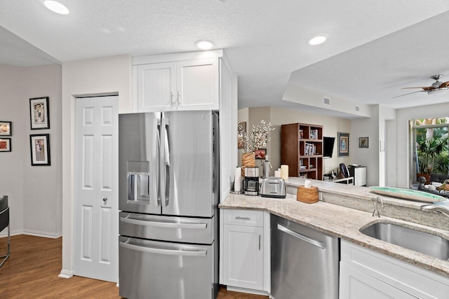 kitchen with a sink, light stone countertops, stainless steel appliances, and white cabinetry