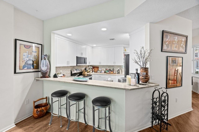 kitchen with a peninsula, appliances with stainless steel finishes, wood finished floors, and tasteful backsplash