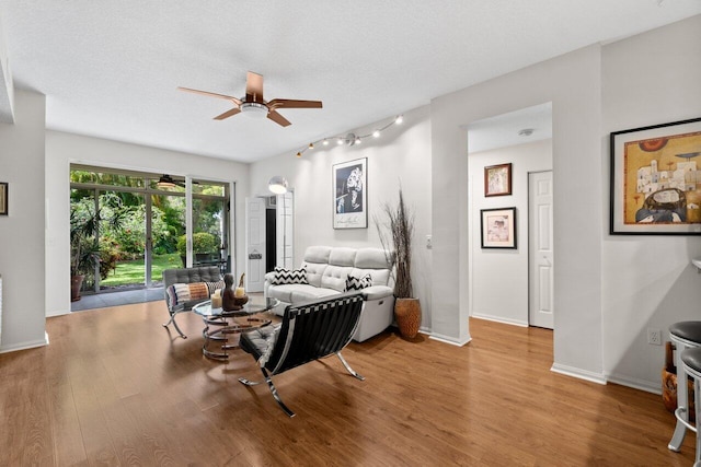 living room featuring baseboards, rail lighting, ceiling fan, and wood finished floors