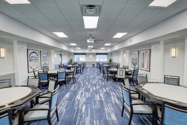 dining space featuring visible vents, a drop ceiling, and dark colored carpet