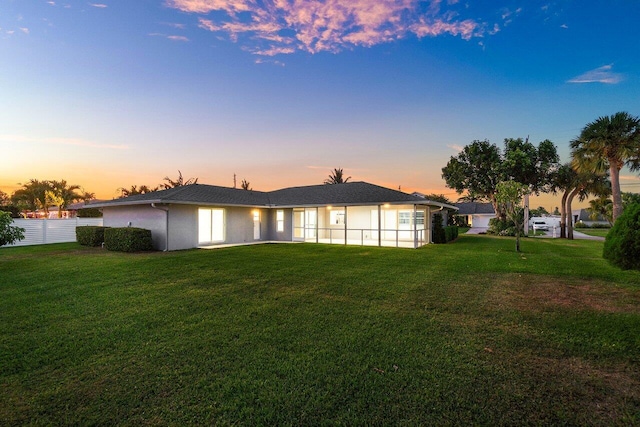 back of property at dusk with a yard, fence, and stucco siding