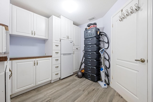 17225 Mare Ln, Loxahatchee, FL 33470 - kitchen with freestanding refrigerator, light wood finished floors, white cabinetry, dark countertops, and a textured ceiling