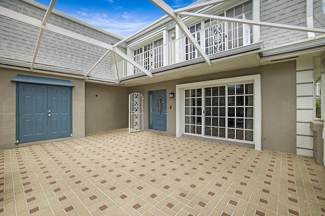 503 Vision Ct, Palm Beach Gardens, FL 33418 - view of exterior entry with roof with shingles, a balcony, a patio area, and stucco siding