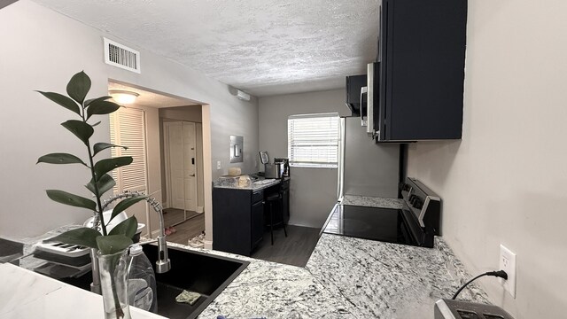2925 SW 22nd Ave Unit 2030, Delray Beach, FL 33445 - kitchen featuring appliances with stainless steel finishes, dark cabinetry, a textured ceiling, wood finished floors, and light stone countertops