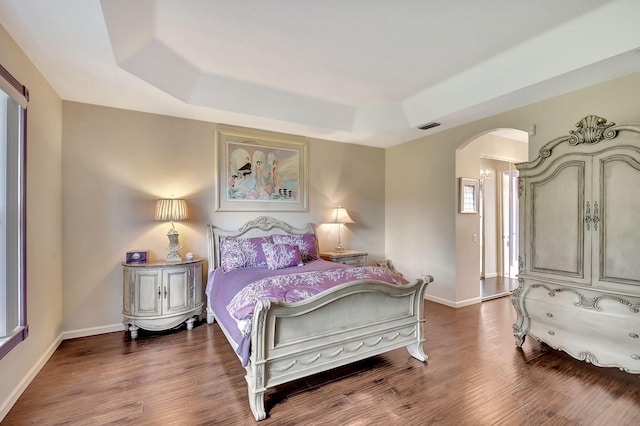 bedroom with arched walkways, baseboards, wood finished floors, a tray ceiling, and visible vents