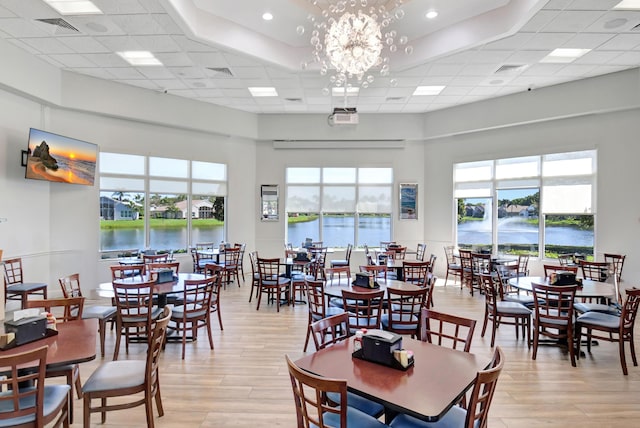 dining area with a water view, visible vents, a paneled ceiling, and light wood finished floors