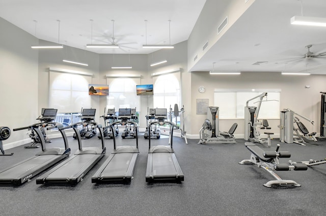 gym featuring a towering ceiling, baseboards, a ceiling fan, and visible vents