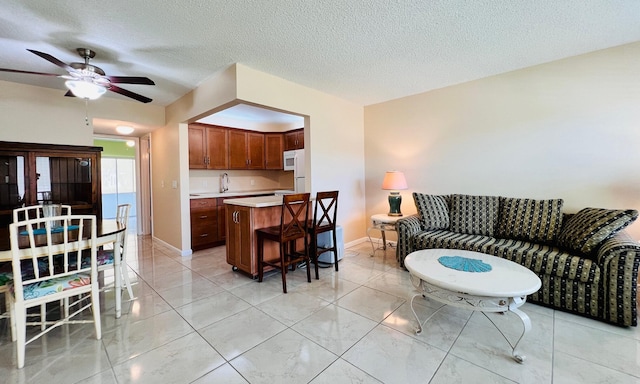 living area with baseboards, ceiling fan, a textured ceiling, and marble finish floor