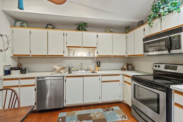 kitchen featuring appliances with stainless steel finishes, a sink, light countertops, dark wood-type flooring, and vaulted ceiling