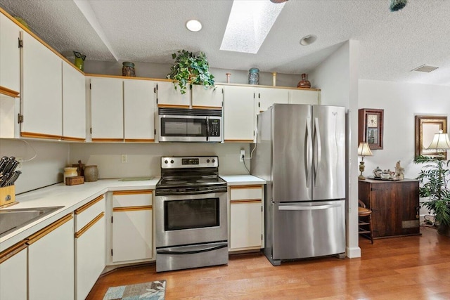 kitchen featuring light countertops, a textured ceiling, light wood-style flooring, stainless steel appliances, and a skylight