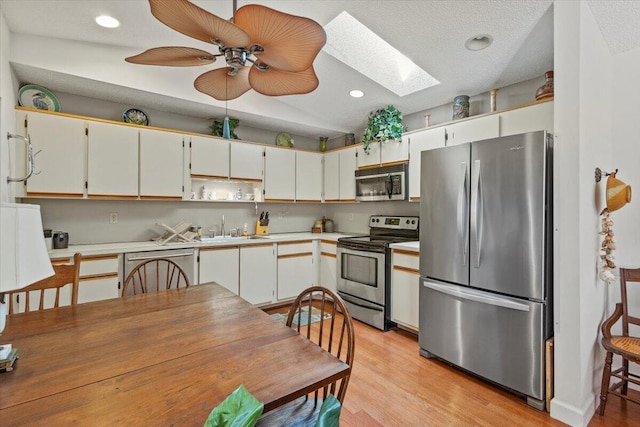 kitchen with open shelves, light countertops, a sink, a skylight, and stainless steel appliances