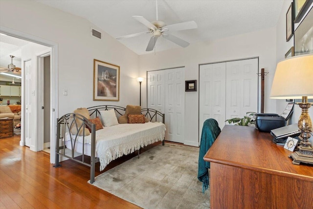 bedroom with visible vents, two closets, wood finished floors, a ceiling fan, and vaulted ceiling