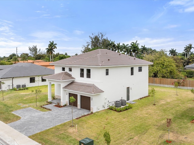back of property with an attached garage, concrete driveway, fence, and a lawn
