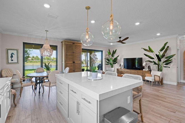kitchen with light countertops, white cabinets, a kitchen island, and ceiling fan with notable chandelier