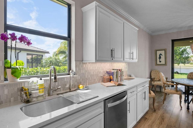 kitchen featuring a sink, dishwasher, light countertops, light wood-type flooring, and ornamental molding