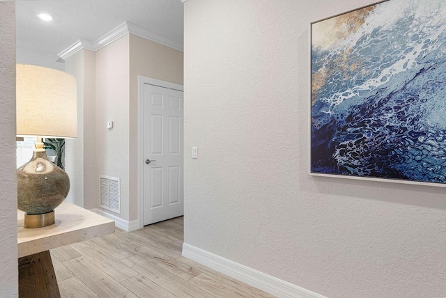 hallway featuring crown molding, a textured wall, baseboards, wood finished floors, and visible vents