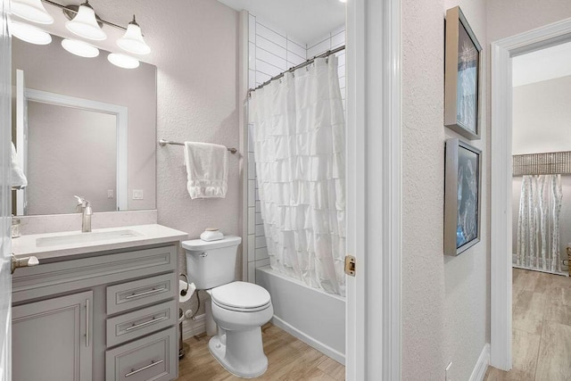 bathroom featuring shower / bath combination with curtain, wood finished floors, vanity, toilet, and a textured wall