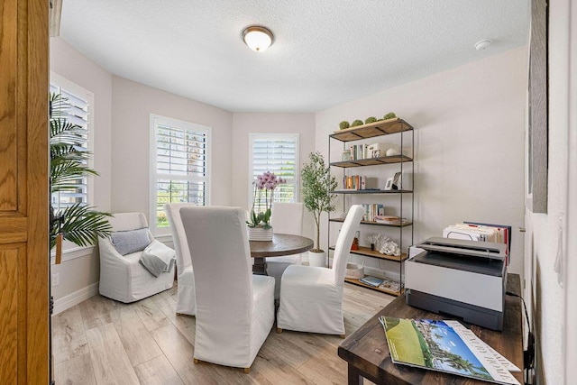 dining space featuring a textured ceiling, baseboards, and light wood-type flooring