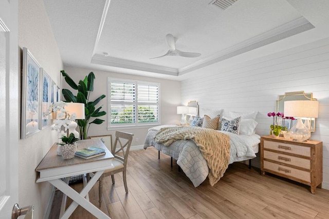 bedroom featuring crown molding, a raised ceiling, light wood-type flooring, and a textured ceiling