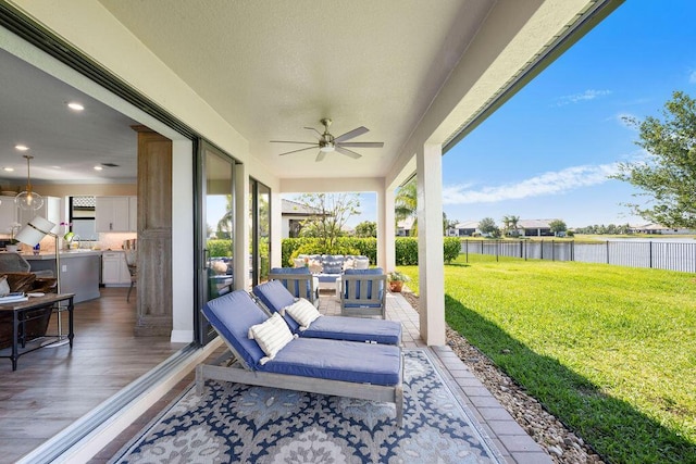 view of patio / terrace with a water view, ceiling fan, an outdoor living space, and a fenced backyard