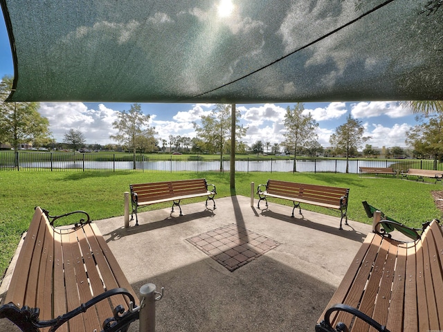 view of home's community with fence, a water view, a lawn, and a patio area